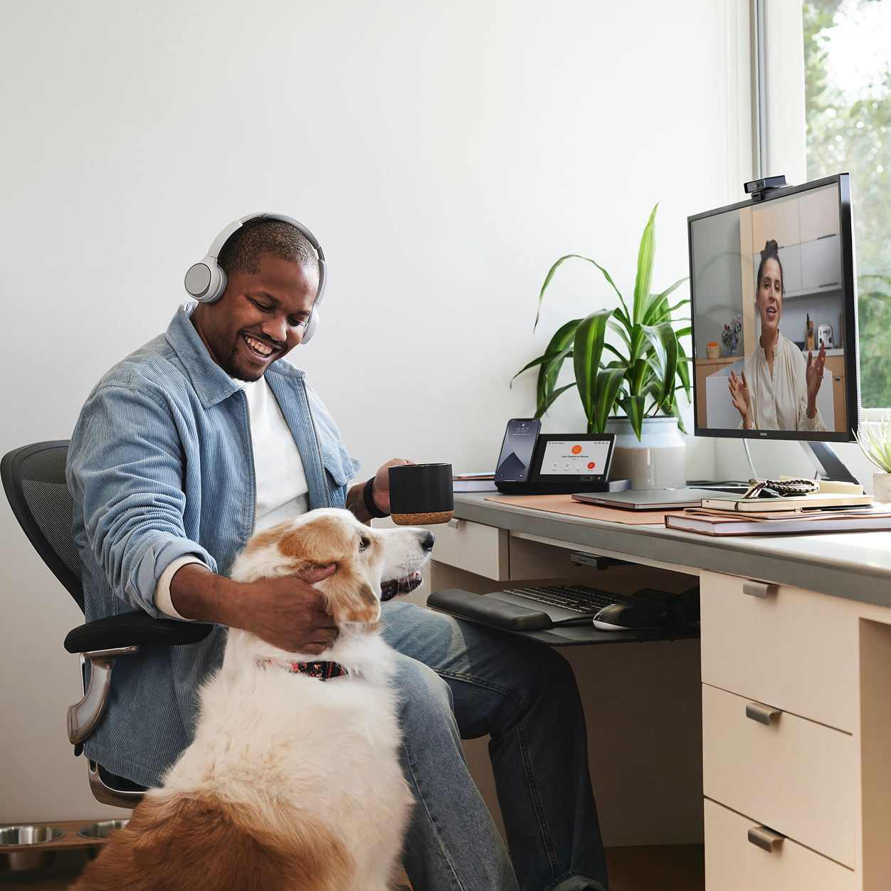 En person med hovedtelefoner sidder og klapper sin hund ved et skrivebord med en skærm, der viser et Webex-møde.